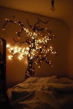 a lighted tree in the corner of a room next to a bed with white sheets