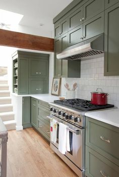 a stove top oven sitting inside of a kitchen next to green cupboards and stairs