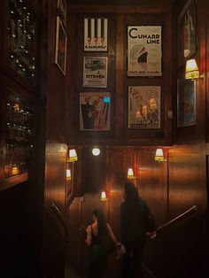 two people are walking up the stairs in a dark room with posters on the wall