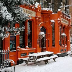 an orange building with snow on the ground and benches around it in front of trees