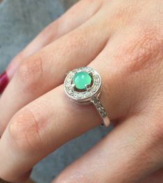 a close up of a person's hand wearing a ring with a green stone