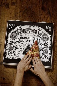 a person holding a slice of pizza on top of a wooden table next to a poster