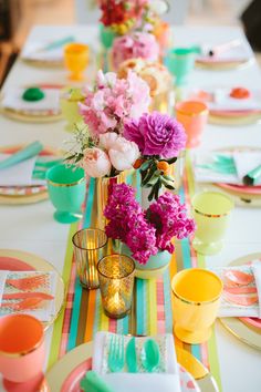 the table is set with colorful plates, cups, and vases filled with flowers