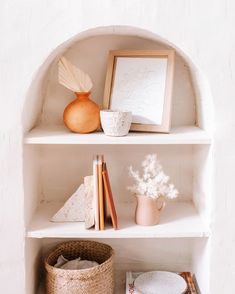 a shelf with books, vases and other items on it in a white room