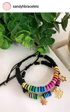 multicolored bracelets with gold charms and star charms on them sitting next to a potted plant