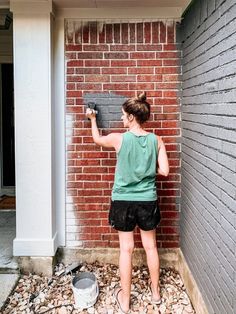 a woman is painting a brick wall outside