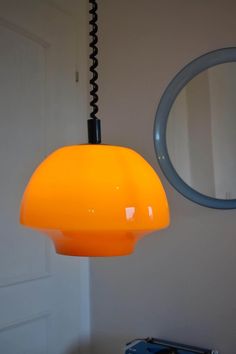 an orange lamp hanging from a ceiling next to a round mirror and blue object on the wall