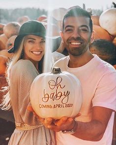 a man and woman standing next to each other holding a pumpkin