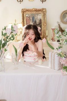 a woman sitting at a table with a cake in front of her and flowers behind her