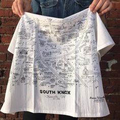 a person holding up a white t - shirt that has a map drawn on it