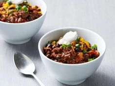 two white bowls filled with chili and sour cream on top of a table next to a spoon