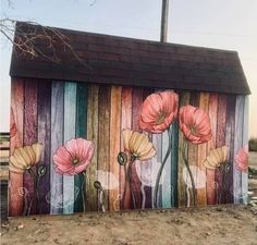 a painted wall with flowers on it and a wooden fence in the foreground, next to a building