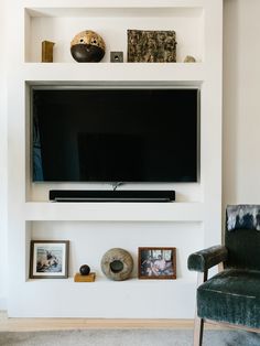 a flat screen tv mounted on a white wall above a shelf filled with pictures and other items