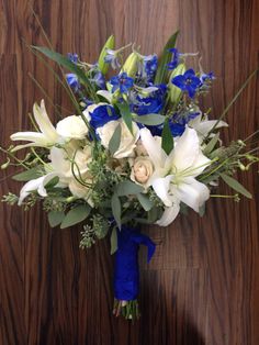 a bridal bouquet with blue and white flowers on a wooden table next to a wall