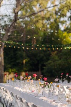 a long table is set up with white linens and floral centerpieces for an outdoor wedding reception