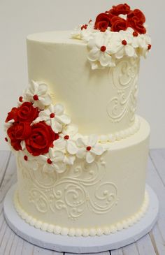 two tiered wedding cake with red and white flowers on each layer, sitting on top of a wooden table