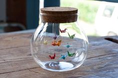 a glass jar filled with tiny origami butterflies on top of a wooden table