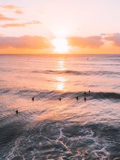 the sun is setting over the ocean with surfers in the water