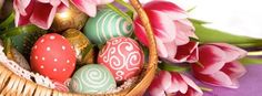 a basket filled with lots of colorful easter eggs next to pink tulips and green leaves