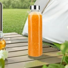 a bottle of orange liquid sitting on top of a wooden table next to a tent