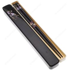 two chopsticks in a black box with flowers on it and gold trimming