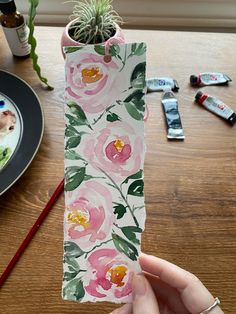 a person holding up a piece of paper with flowers on it and succulents in the background