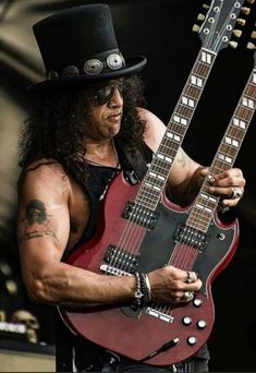 a man with long hair and a top hat is playing an electric guitar on stage