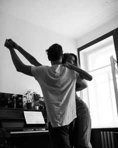 a man and woman are dancing together in front of a piano with their arms around each other