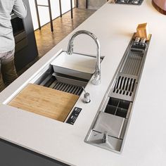 a kitchen counter with a sink and wooden cutting board on it, in front of a woman