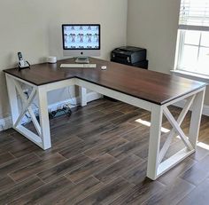 a desk with a computer on it in front of a window and hardwood flooring