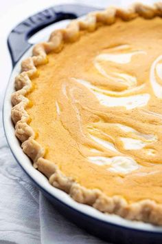 a pumpkin pie with white frosting in a pan on top of a tablecloth