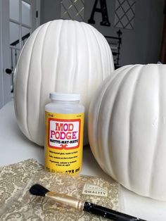 some white pumpkins sitting on top of a table next to a paint bottle and brush