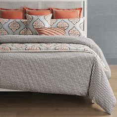 a bed with orange and gray pillows on it in a bedroom next to a white headboard