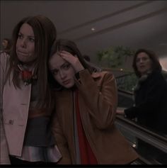 two women standing next to each other on an escalator with their hands in their hair