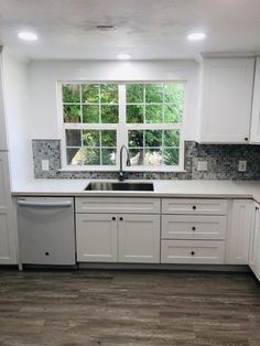 an empty kitchen with white cabinets and gray tile backsplash, wood flooring