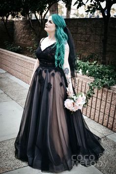 a woman with long green hair wearing a black dress and holding flowers in her hand