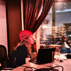 a woman sitting at a table with a laptop in front of her and another person behind her