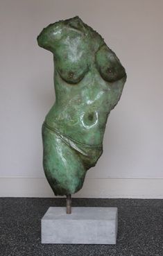 a green sculpture sitting on top of a white pedestal next to a gray wall and floor