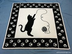 a black and white knitted rug with a cat playing with a ball of yarn