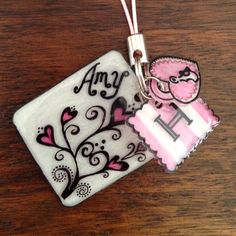 two ceramic tags with pink and black designs are on a wooden table, one has a monogram in the middle