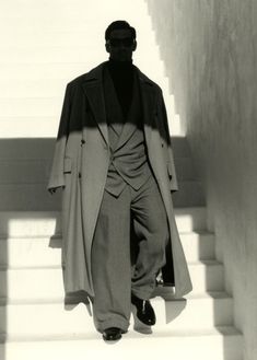 a man in a long coat and hat walking down the stairs with his hands on his hips