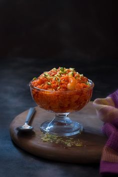 a bowl filled with food sitting on top of a wooden table next to a spoon