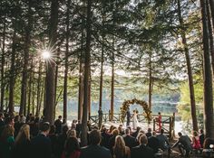 a wedding ceremony in the woods with sun shining through the trees and onlookers