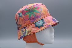 a white mannequin head wearing a pink hat with colorful flowers and butterflies on it