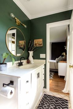 a bathroom with dark green walls and white cabinets, black and white rugs on the floor