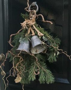 two bells hanging from a door with pine needles and twine around them on the front door