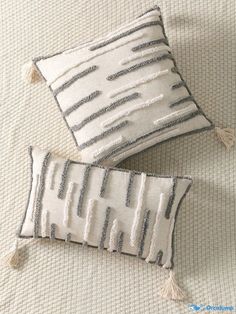 two decorative pillows with tassels are on a bed together, one is white and the other is gray