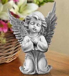 an angel statue sitting on top of a wooden table next to a basket of flowers