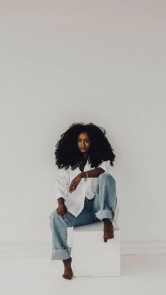 a woman sitting on top of a white block wearing jeans and a white button up shirt