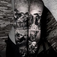 a man's leg with tattoos on it and mountains in the background, while he is